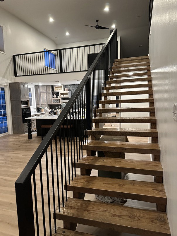 Elegant wooden staircase with black metal railings, painted by Adel Painting Contractor Phillips Pro Painting, leading to an open-plan loft area.