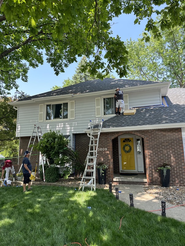 Adel's Top Painters at work on a two-story home, with ladders against the siding and a vibrant yellow door.